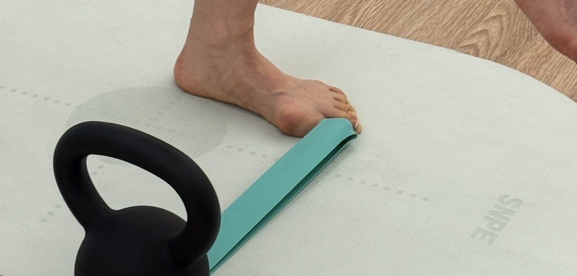 밴드를 발가락에 걸고 한 발로 서서 발과 발목의 움직임을 조절하는 모습